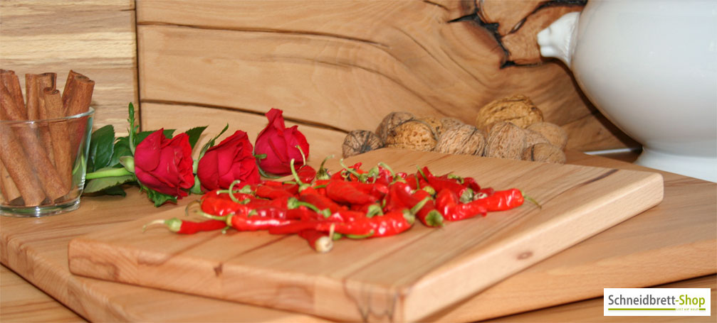 Holzbretter Buche mit scharfen Chilischoten liegen vor Rosen, Nüssen und Zimtstangen.